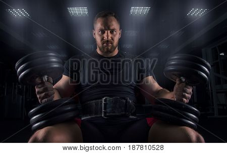Impressive Athlete Sits On A Bench With Two Dumbbells On His Legs