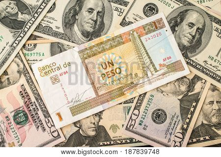One Cuban pesos bill over several dollar bills