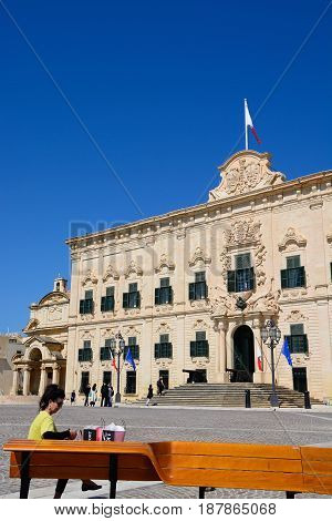 VALLETTA, MALTA - MARCH 30, 2017 - View of the Auberge de Castille in Castille Square with a woman sitting on a bench looking at her shopping in the foreground Valletta Malta Europe, March 30, 2017.