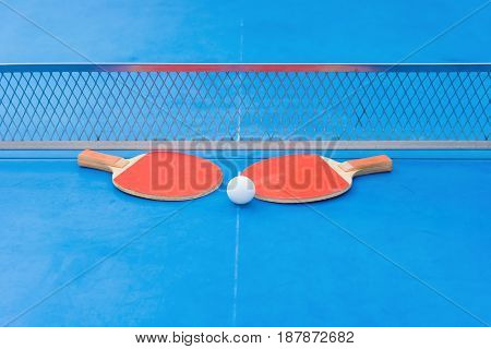 pingpong rackets and ball and net on a blue pingpong table