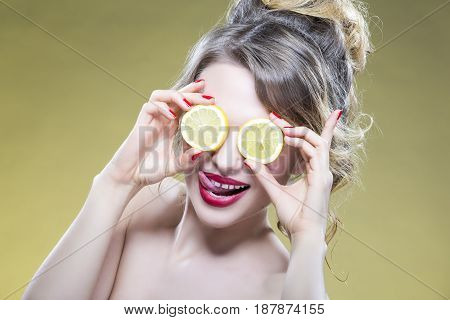 Sexy Fruit Series. Closeup Portrait of Cute Funny Naked Caucasian Girl Holding A Pair of Lemon Slices In Front of Her Eyes with Smile. Against Yellow. Horizontal Image Composition