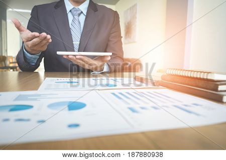 Handsome young businessman working with touchpad while sitting on the couch in office and financial statistic graph.