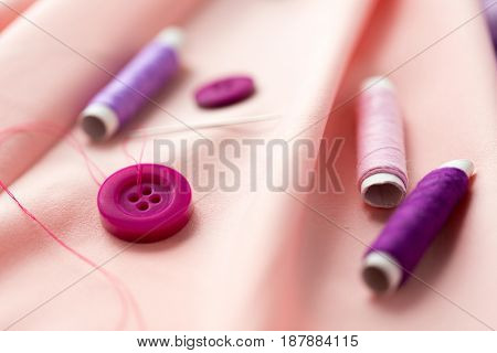 needlework and tailoring concept - sewing buttons, spools of thread and cloth