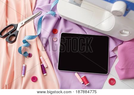 needlework, technology and tailoring concept - sewing machine with tablet pc computer, scissors, tape measure and fabric