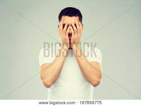 people, crisis, emotions and stress concept - man in white t-shirt covering his face with hands over gray background
