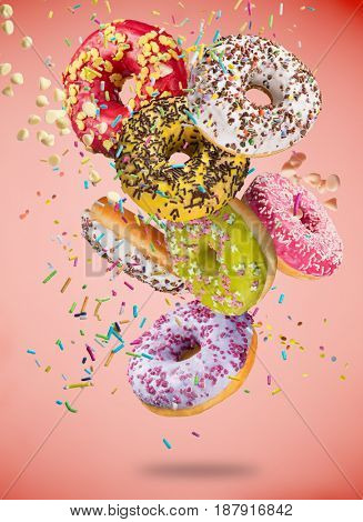 Tasty donuts in motion falling on pastel red background, close-up.