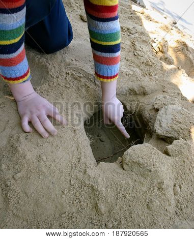 The child is on the street. Playing on the court. A hole is dug. In it the roots of the plant. The finger points to the pit. Yellow background.