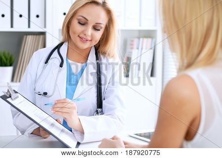 Doctor and  patient  discussing something while phisician pointing into medical history form at clipboard. Medicine and health care concept
