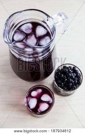 Blueberry juice in a decanter and a glass next to frozen berries