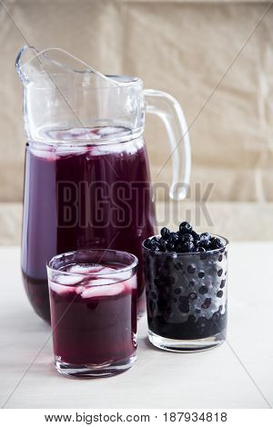 Blueberry juice in a decanter and a glass next to frozen berries