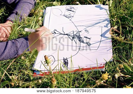 Close Up View Of Child's Hand Drawing Colorful Ornaments On Paper. Notebook In Fresh Green Grass Of 