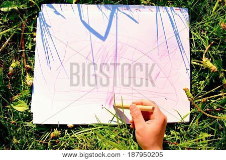Close Up View Of Child's Hand Drawing Colorful Ornaments On Paper. Notebook In Fresh Green Grass Of 