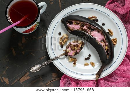 Bananas baked in peel on grill with chocolate drops and marshmallow. Black peel serves as natural pot for delicious banana dessert. Dessert is served hot sprinkled with walnuts. Eat with spoon
