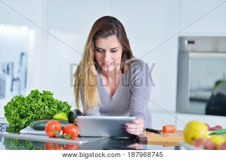 Young woman is making online shopping by tablet computer. Housewife found new recipe for cooking in a kitchen.