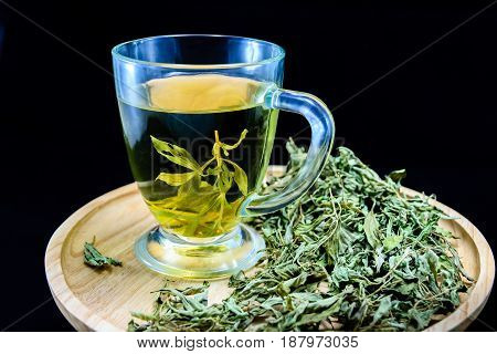 Dry stevia leaves with a cup with stevia infusion on wooden tray on black background
