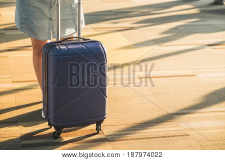 Young casual woman wear white sneakers standing with travel suitcase with morning sunlight through window at airport terminalVacation concept.