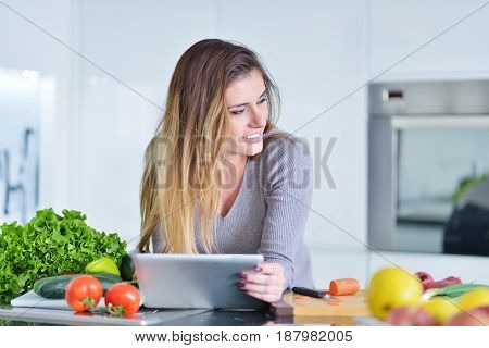 Young woman is making online shopping by tablet computer. Housewife found new recipe for cooking in a kitchen.