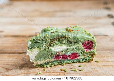 Piece of green pistachio cake with red berries on wooden background
