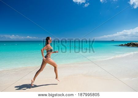 Young pretty sexy woman with beautiful body in swimsuit running in ocean water sunny day at tropicl beach wellness concept