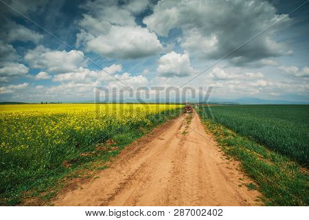 Red Tractor Working In A Field And Dramatic Clouds