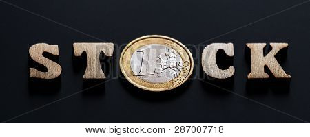The Word Stock Of Wooden Letters With A Coin Of One Euro Instead Of The Letter O. Black Textural Bac