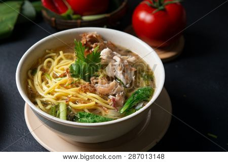 Asian soup noodles and chicken in bowl on dark background. 