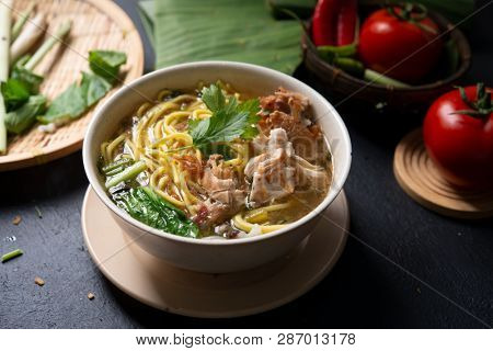 Asian soup noodles and chicken in bowl on dark background. 
