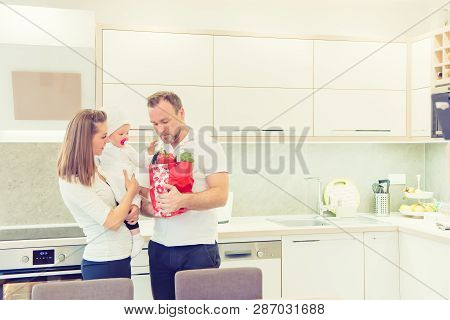 Happy Parents Standing In The Kitchen And Prepares For Cooking With Their Baby Girl Chef. Father Bri
