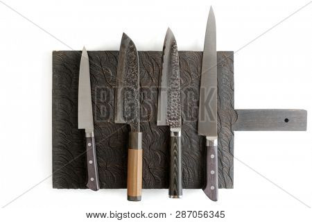 Four different knives on black cutting board, isolated on white with shadows