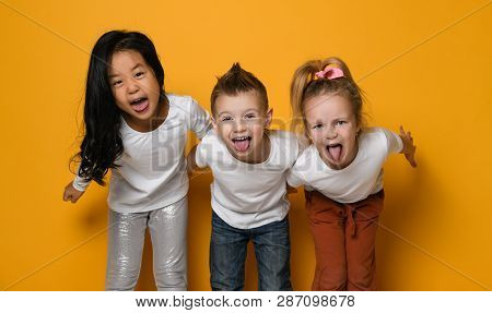 Group Of Funny Children Of Different Races Show Their Tongue To The Camera. Isolated On Yellow Backg