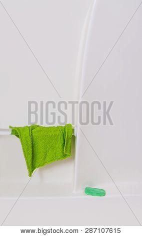 Vertical Close-up Shot Of The Wall Of A White Bathtub.  Green Washcloth Hanging From Handrail And Gr