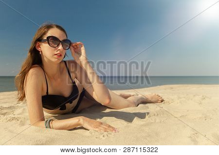 Beautiful Young Woman In Swimsuit At Sand Sea Beach Under Light Rays, Looking At Camera
