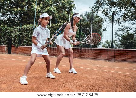 Tennis Training. Cheerful Mother In Sports Clothing Teaching His Daughter To Play Tennis While Both 