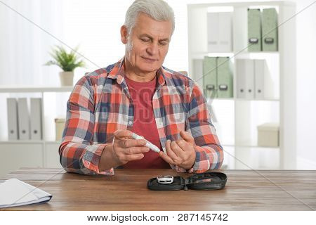 Senior Man Using Lancet Pen At Table. Diabetes Control