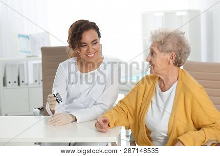 Doctor Checking Patient's Blood Sugar Level With Digital Glucometer At Table. Diabetes Control