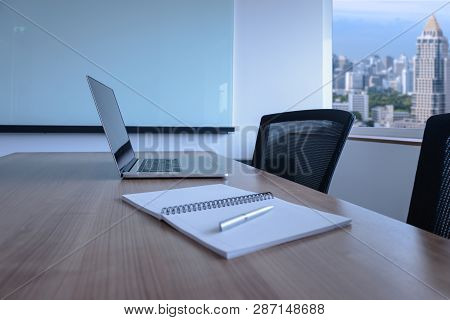 Laptop And Pen On Notepad For Agenda Kept On Table In Empty Corporate Conference Room With Cityscape