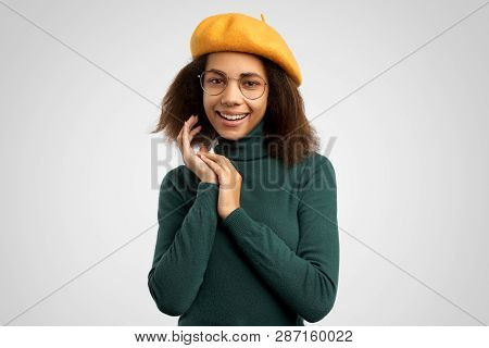 Beautiful Young Joyful Woman Keeps Hands Together, Has Brown Eyes Full Of Happiness, Stands Against 