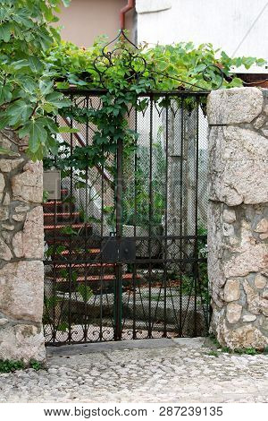 Decorative Wrought Iron Front Yard Entrance Doors Mounted On Traditional Stone Wall Covered With Cra