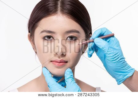 Surgery Concept. The Doctor Is Drawing A Pencil On The Patient's Face. The Patient Is Confident In T