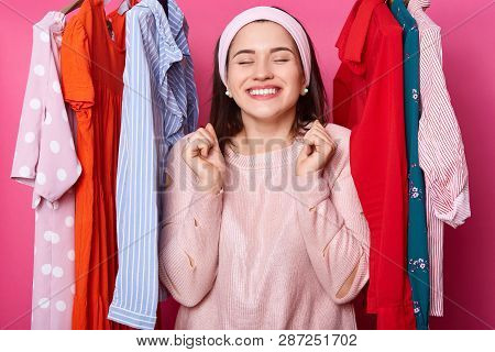 Positive Cheerful Gorgeous Female With Closed Eyes In Boutiqe. Lots Hangers With Outfits. Smiling La
