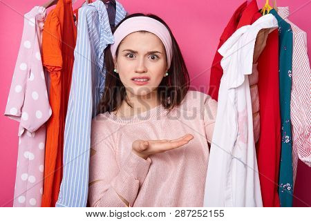 Displeased Female Shows White Shirt, Being Dissatisfied With Size. Girl Stands At Clothes On Hangers