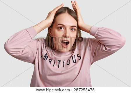 Emotional Stupefied Young Female Keeps Both Hands On Head, Feels Stunned And Impressed To Hear Shock