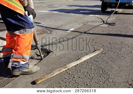 A Road Maintenance Worker Removes Old Asphalt On The Roadway With A Jackhammer Into An Excavator Dur