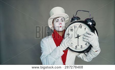 Mime In A Suit And Hat Is Holding A Big Clock. Man In A Suit With A Dial In His Hands. Actor With A 