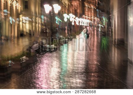 Late Evening In The Deserted City, Lonely Pedestrians Rush Home, Rainy Late Evening. Bright Illumina