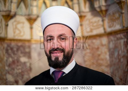 Emam in mosque with verses from Kuran on the wall