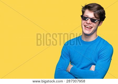 Young man wearing funny thug life glasses over isolated background happy face smiling with crossed arms looking at the camera. Positive person.