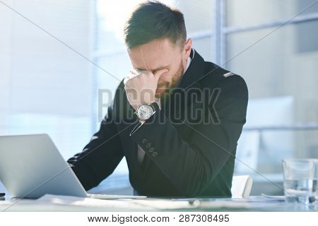 Tense and tired young businessman in formalwear trying to concentrate while sitting in front of laptop in office