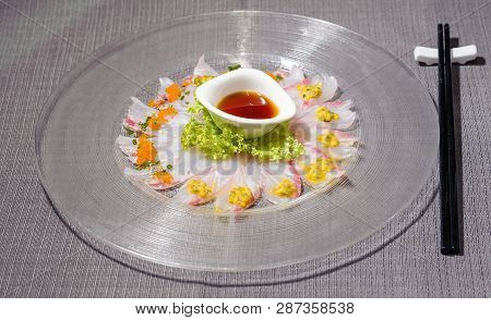 Fresh Amberjack Carpaccio With Salad And Citrus Fruit Sauce Served On A Big Rounded Glass Dish