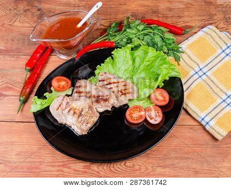 Top View Of The Grilled Pork Steaks On Lettuce Leaves And Cherry Tomatoes On Black Dish, Souce, Gree
